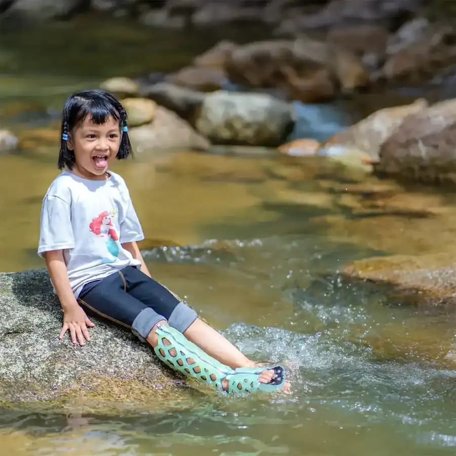 A child with a green FlexiOH leg cast sitting in a stream