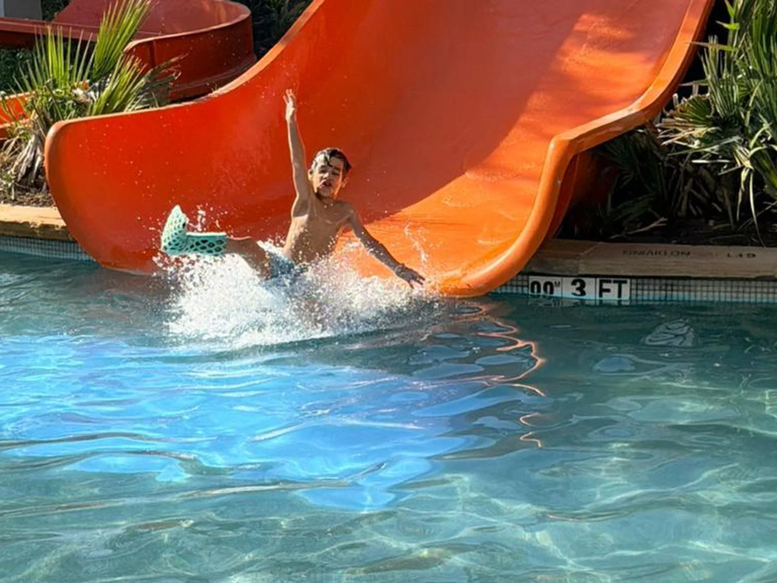 A child with a FlexiOH cast splashing off a waterslide into a pool